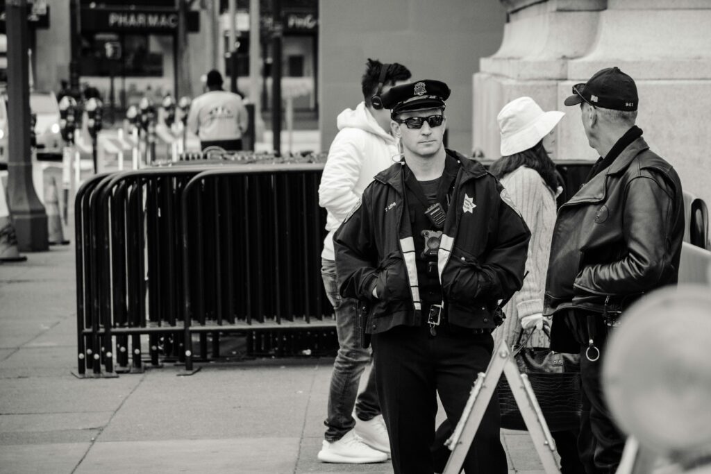 A police officer on patrol in an urban street, engaging in conversation, captured in black and white.